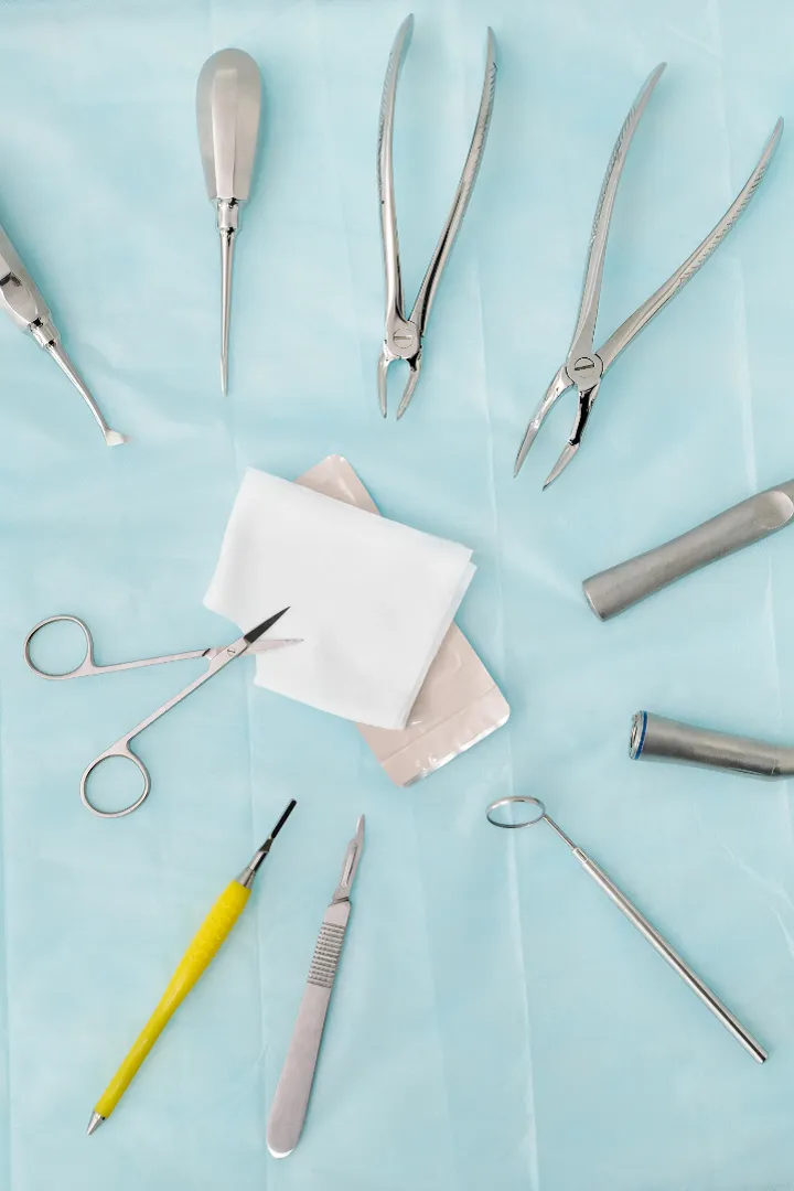 A set of dental instruments, including pliers, scissors, syringes, and mirrors, arranged on a light blue cloth