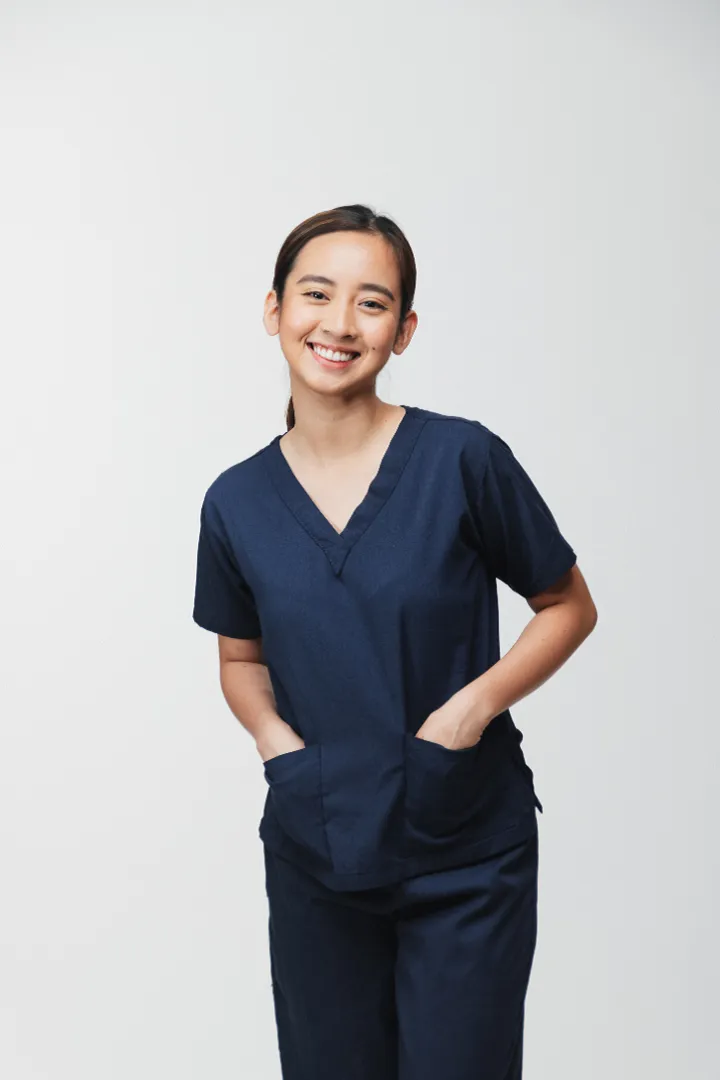 A woman dentist smiling and wearing navy blue medical scrubs with hands in pockets