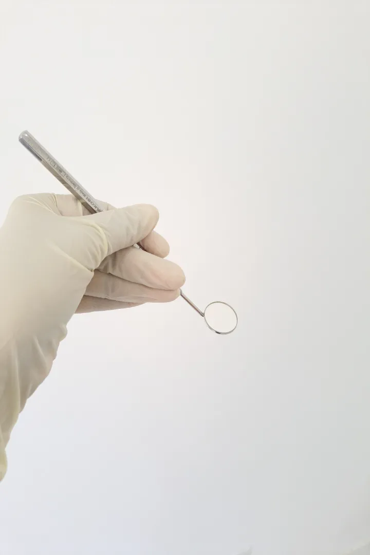 Hand in a latex glove holding a dental mirror against a white background