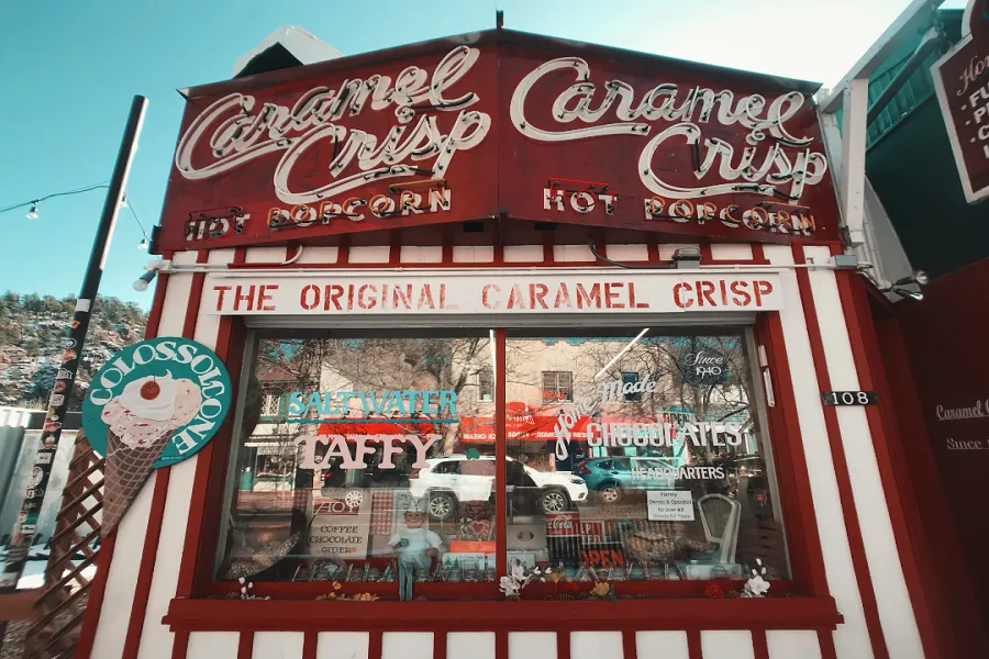 A charming candy shop facade featuring bright red and white stripes, boasting Caramel Crisp signage and offerings like popcorn and taffy